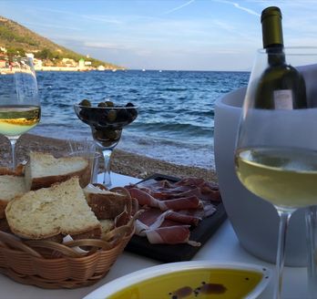 Ein Glas Weißwein und eine Platte mit Schinken am Meer.