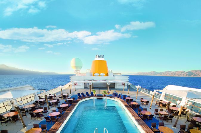 Ein Swimmingpool-Bereich auf einem Kreuzfahrtschiff mit Blick auf eine Stadt.