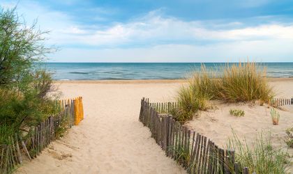 Ein Holzpfad führt über Sanddünen zum Strand in Languedoc-Roussillon, Frankreich, mit Meer und blauem Himmel.
