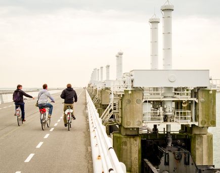 Zwei Personen fahren Fahrrad auf einem Weg, der zu einem Hafen führt.