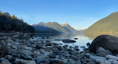 Alouette Lake bei Golden. Kleine Felssteine ragen in den See, zu sehen die schneebeckten Rocky Mountains im Hintergrund und Bäume.