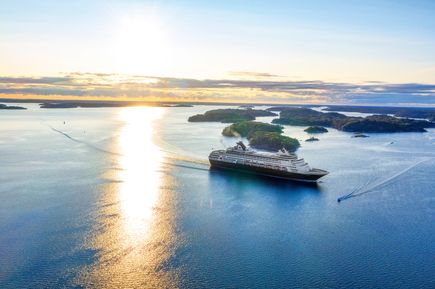 Ein Kreuzfahrtschiff liegt in einem Fjord mit Blick auf die Stadt bei Sonnenuntergang.