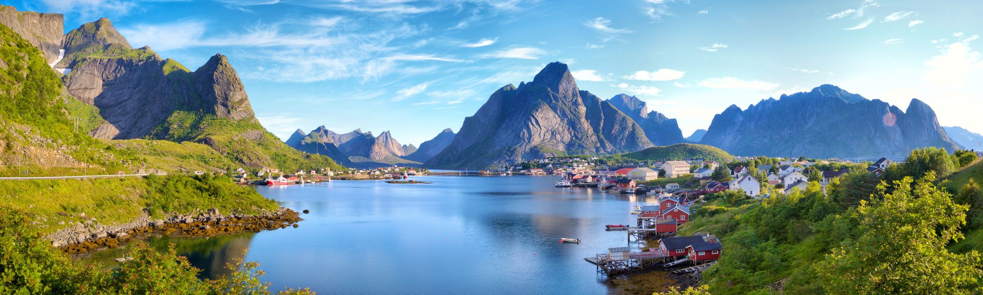 Eine atemberaubende Landschaft der Lofoten in Norwegen, zeigt das malerische Dorf Reine mit seinen roten Fischerhütten, umgeben von majestätischen Bergen, die sich aus dem Meer erheben.
