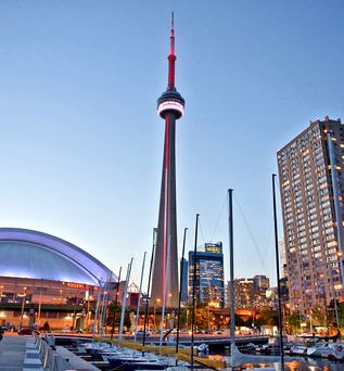 Die hell erleuchtete Skyline von Toronto bei Nacht, mit dem markanten CN Tower und dem Rogers Centre Stadion, gesehen von einem erhöhten Aussichtspunkt über der Stadt.