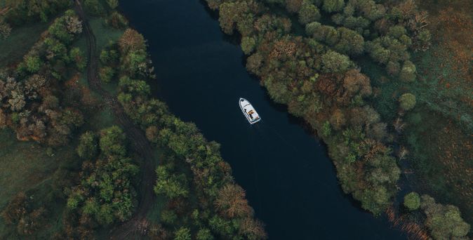 Luftaufnahme einer kleinen Insel mit Ruinen einer Burg im ruhigen See, davor ein Boot – umgeben von herbstlicher Landschaft.