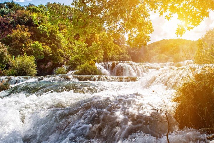 Eine Landschaft mit einem Wasserfall und Gebäuden bei Sonnenuntergang.