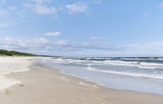 Ein breiter Sandstrand an der Ostsee mit Wellen, Dünengras und einem bewölkten Himmel, in Damp, Deutschland.