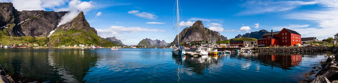 Panoramablick auf das Fischerdorf Hamnøy auf den Lofoten, Norwegen, mit roten Fischerhütten (Rorbuer) am Ufer, Booten im klaren Wasser 