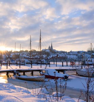 Die Stadt Flensburg in Norddeutschland bei Sonnenuntergang mit Segelbooten in gefrorenem Wasser und Schnee