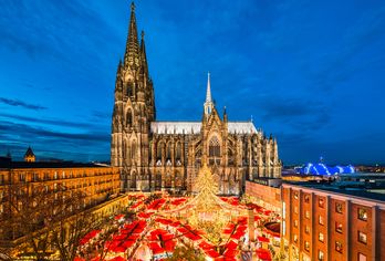 Stimmungsvoller Weihnachtsmarkt mit leuchtenden Ständen vor der majestätischen Kulisse des Kölner Doms bei Abenddämmerung.