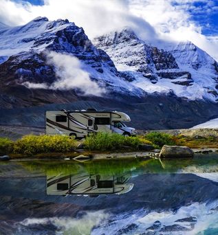 Camper steht am See mit Bergen im Hintergrund