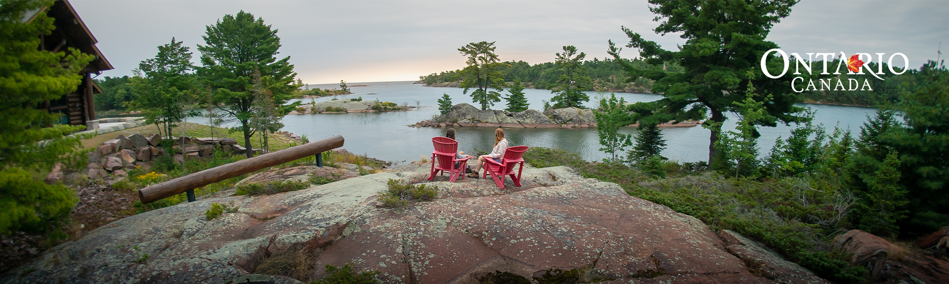 2 Personen sitzen auf roten Stühlen auf einem Hügel mit Blick in die Weite