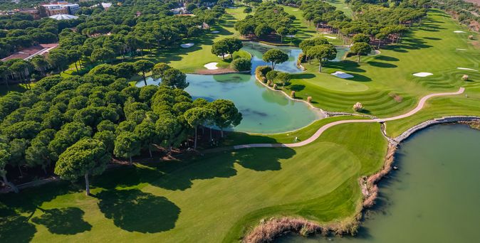 Luftaufnahme eines weitläufigen Golfplatzes in Belek, Türkei, mit sorgfältig gepflegten grünen Fairways, Bäumen und einem Wasserhindernis, das sich durch die Landschaft schlängelt.
