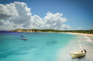 Playa Macao: Zwei kleine Boote im klaren Wasser einer ruhigen Badebucht mit weitem Sandstrand und tropischer Küstenlandschaft.