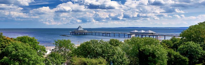 Blick auf Usedom mit seinen Bäumen, einer Promenade und einem Steg welcher ins Wasser reicht.