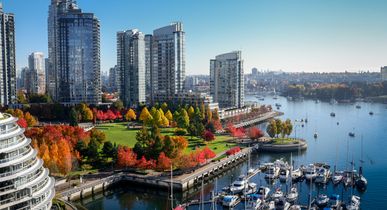 Blick auf Vancouver, den kleinen Hafen mit vielen Booten im Wasser. Hohe Gebäude, Garten mit Bäumen in Herbstfarben, Weitsicht über den Rest der Stadt.
