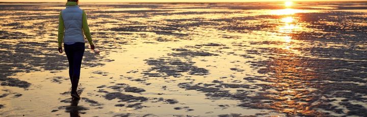 Eine Person geht auf einem Strandweg bei Sonnenuntergang.