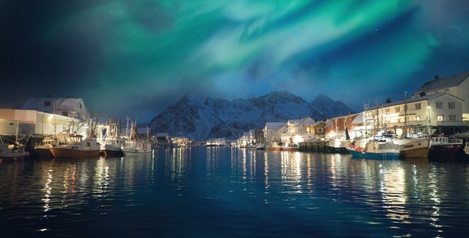 Blick auf den Hafen von Tromso bei Nacht mit einigen Schiffen im Vordergrund und im Hintergrund schneebedeckte Berge
