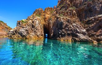 Die beeindruckenden roten Felsformationen der Calanques de Piana in Korsika, Frankreich, die steil aus dem türkisblauen Meer aufragen, umgeben von üppiger Vegetation.