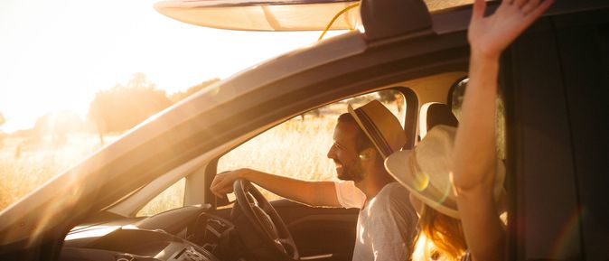 Eine Person fährt Auto, mit Surfbrettern auf dem Dach, bei Sonnenuntergang.