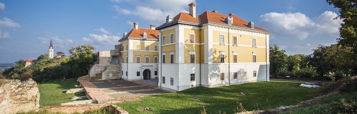 Ein Schloss oder Herrenhaus auf einem Hügel, umgeben von grüner Landschaft.