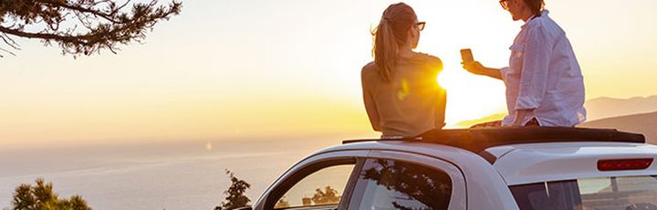 Paar sitzt auf einem Auto mit Sonnenuntergang im Hintergrund