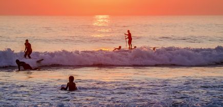 Eine Person surft bei Sonnenuntergang am Strand, mit Blick auf das Meer.