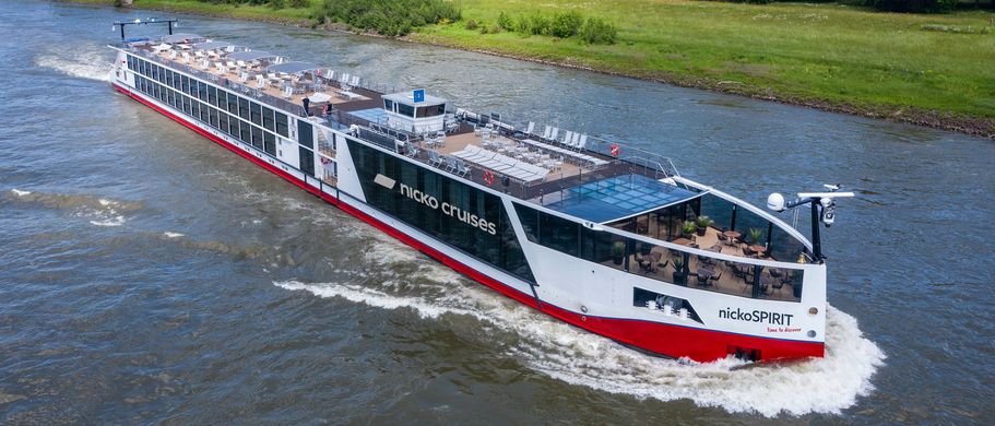 Ein Flusskreuzfahrtschiff fährt auf einem Fluss, umgeben von grünen Ufern.