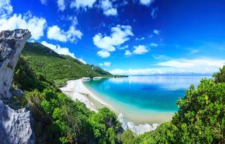 Eine Küstenlandschaft mit einem Strand, Bergen und türkisfarbenem Wasser.