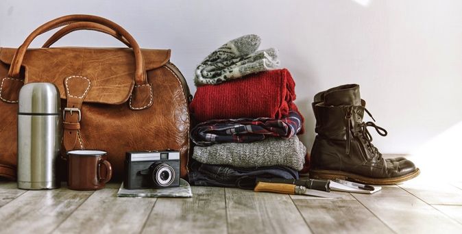 Ein brauner Lederrucksack, eine Kamera und andere Reiseutensilien.