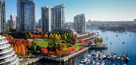 Blick auf Vancouver, den kleinen Hafen mit vielen Booten im Wasser. Hohe Gebäude, Garten mit Bäumen in Herbstfarben, Weitsicht über den Rest der Stadt.