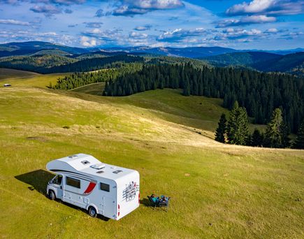 Camper auf einer weitläufigen Wiesenfläche in Transilvanien. Im Hintergrund hügelige Waldlandschaft und strahlend blauer Himmel.