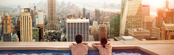 Paar blickt im Infinity-Pool über eine Großstadt 