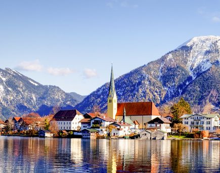 Eine Stadt am Ufer eines Sees, umgeben von schneebedeckten Bergen, Bayern.