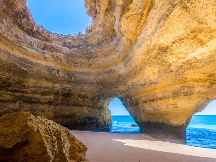 Eine natürliche Höhle mit einem Bogen, der zum Meer führt, beleuchtet von der Sonne.