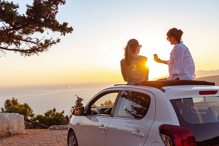 Paar sitzt auf einem Auto mit Sonnenuntergang im Hintergrund