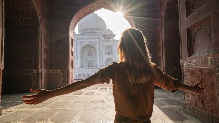 Eine junge Frau in einem Sari posiert vor dem majestätischen Taj Mahal in Indien, der sich unter einem bewölkten Himmel erhebt.