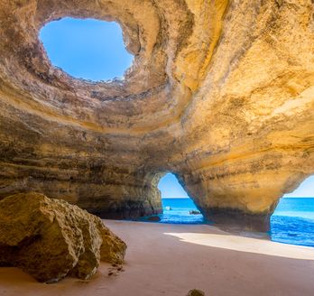 Eine natürliche Höhle mit einem Bogen, der zum Meer führt, beleuchtet von der Sonne.