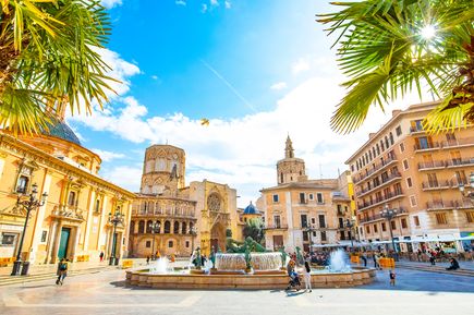 Belebter Platz in Valencia mit Brunnen, Kathedrale und Palmen unter blauem Himmel