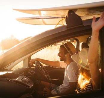 Eine Person fährt Auto, mit Surfbrettern auf dem Dach, bei Sonnenuntergang.