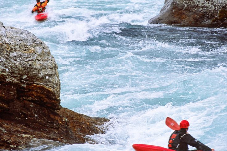 Ein Schlauchboot mit Personen auf einem Fluss, umgeben von Stromschnellen.