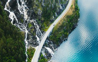 Eine Luftaufnahme einer gewundenen Bergstraße, die sich durch grüne Vegetation und einen Fluss schlängelt.