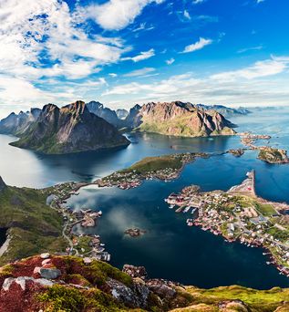 Ein weißer Campervan parkt an einem Seeufer mit Blick auf einen Fjord und Berge unter blauem Himmel.