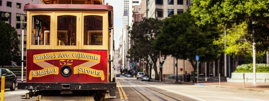 Historische Kabelstraßenbahn in San Francisco fährt eine leere Innenstadtstraße entlang, umgeben von Hochhäusern und Bäumen.