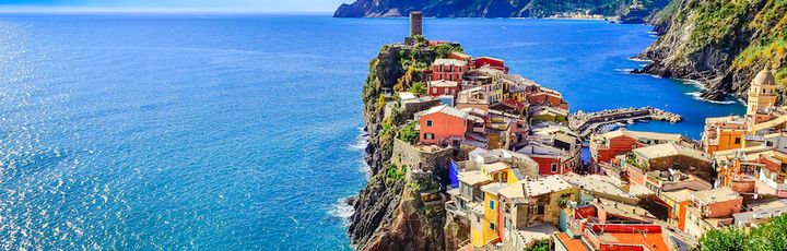 Panoramablick auf das bunte Küstendorf Vernazza, Cinque Terre, Italien, mit Hafen, Häusern am Hang und einem Leuchtturm.