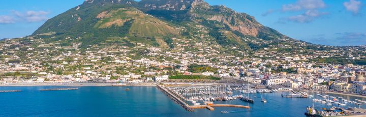 Blick aus der Vogelperspektive auf den Monte Epomeo. Davor die Stadt und davor kleine Boote im Meer.