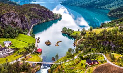 Eine Luftaufnahme einer gewundenen Bergstraße, die sich durch grüne Vegetation und einen Fluss schlängelt.