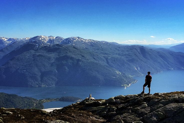 Eine Person steht auf einem Bergkamm und blickt über eine weite, bergige Landschaft in Norwegen.
