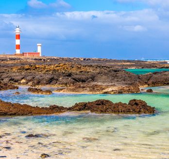 Leuchtturm hinter den Felsen und dem Meer.