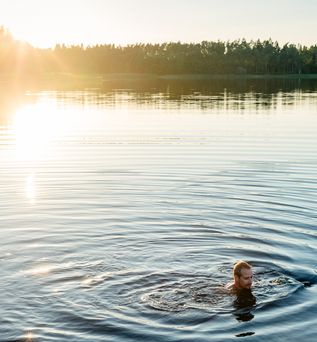 Eine Person schwimmt in einem See bei Sonnenuntergang.
